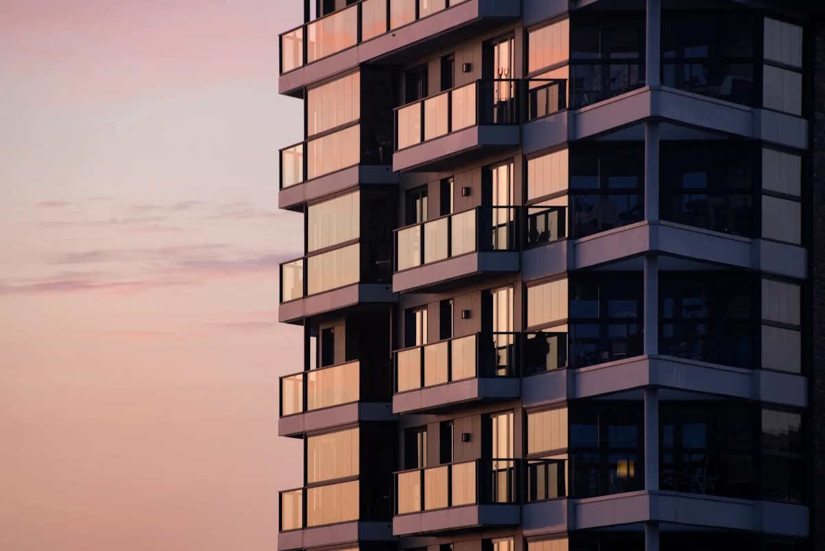 A modern apartment building with glass balconies reflecting a soft pink sky